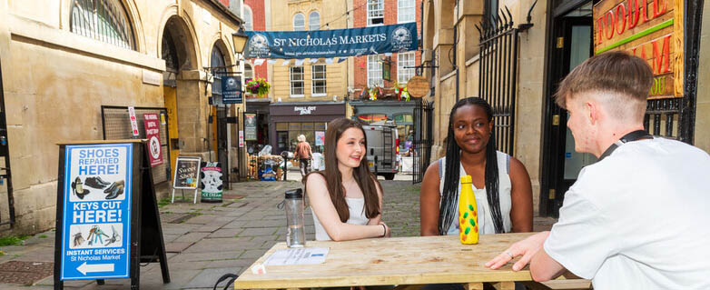 students sit at a wooden table outside st nicks market